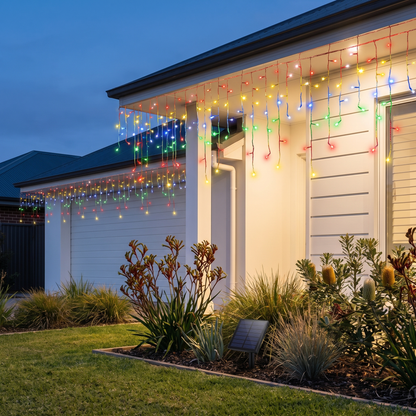 Multicolour Solar LED Icicle Christmas Lights – 12.5m, 500 LED – glowing in a front garden at dusk