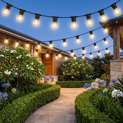 Warm White LED Festoon Christmas String Lights – 23m, 20 Bulbs – glowing along a coastal garden path at twilight
