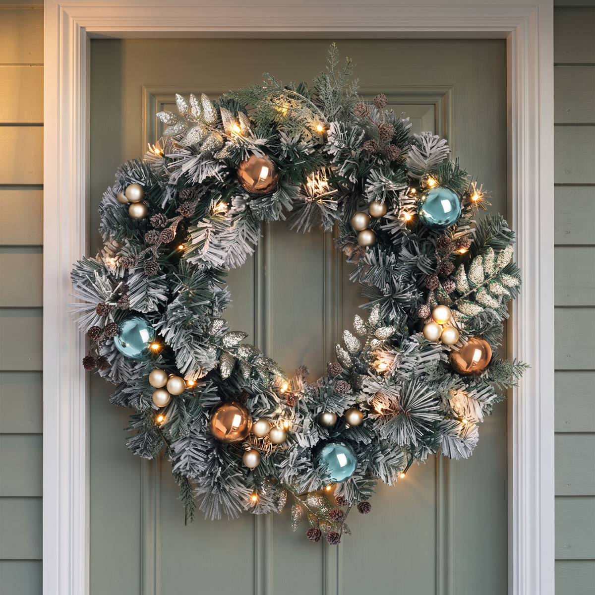 Snow-Frosted Pre-Lit Christmas Wreath – 60cm, 40 Warm White LED – glowing on a sage-green front door at dusk
